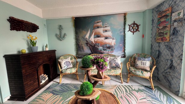 A room with a fireplace, two wicker chairs, a large ship painting, and a wall with nautical decorations. - Doña Lucía (Guánica)