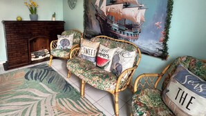 A room with a large ship painting, a wooden chest, and a wicker sofa with floral cushions. - Doña Lucía (Guánica)