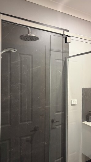 Ducha con cerramiento de vidrio, cabezal de ducha de mano y grifo empotrado.