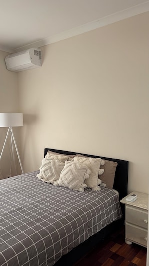 A bedroom with a bed, bedside table, lamp, and an air conditioning unit. - Room-cozy Studio Retreat in Saint Albans (Melbourne)