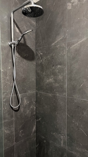 A shower with a handheld attachment, mounted on a wall with dark, textured tiles. - Room-cozy Studio Retreat in Saint Albans (Melbourne)