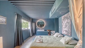 Una camera da letto con un letto, uno specchio rotondo, una finestra, un lavandino e un quadro.
