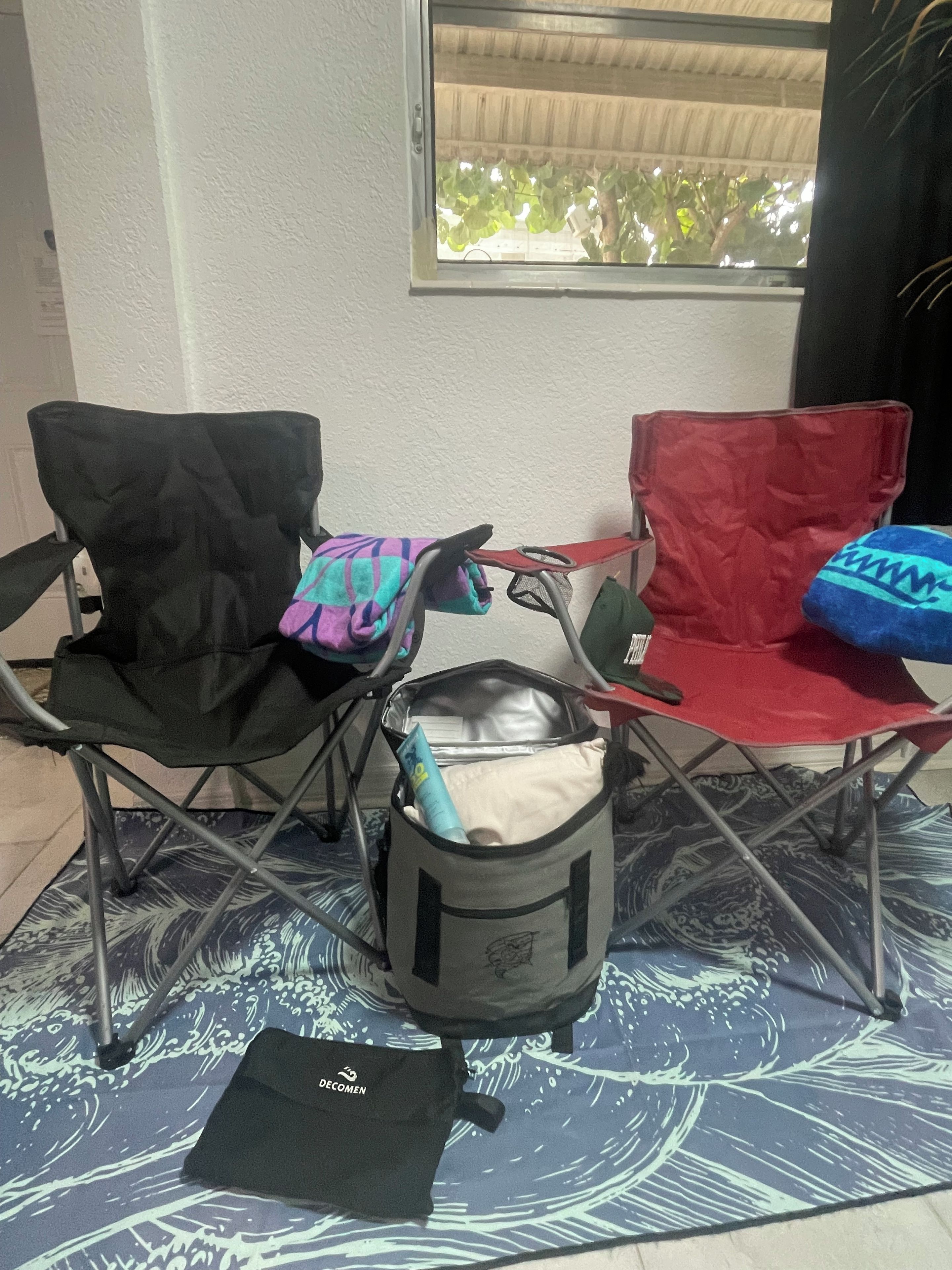 Una habitación con dos sillas plegables, una negra y otra roja, y una bolsa gris con un objeto azul en su interior.