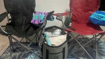Una habitación con dos sillas plegables, una negra y otra roja, y una bolsa gris con un objeto azul en su interior.