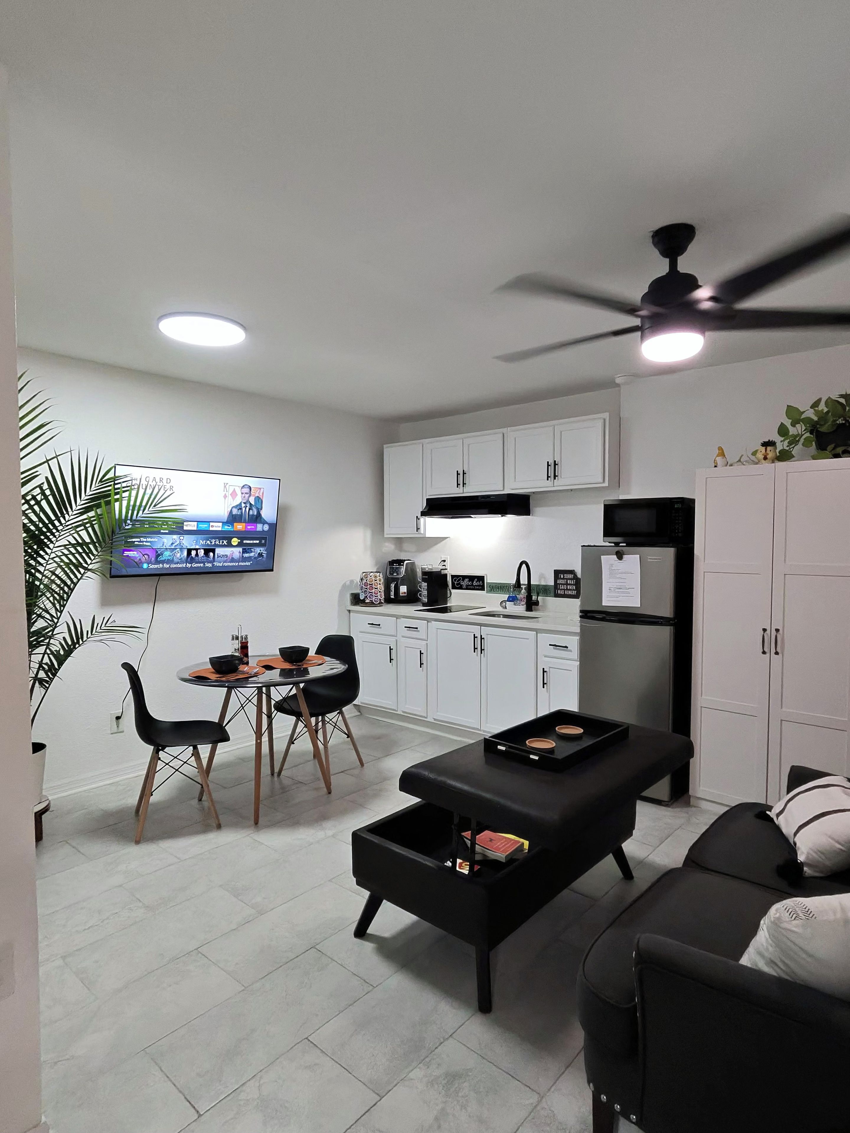 Een compacte leefruimte met een eethoek, kitchenette en een aan de muur bevestigde televisie.