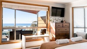 Een slaapkamer met een groot raam, een bed, een bureau, een dressoir en een televisie.