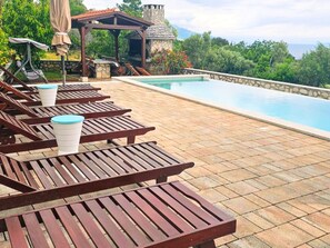 A poolside area with wooden lounge chairs and a stone wall. - Valerija by Interhome (Labin)