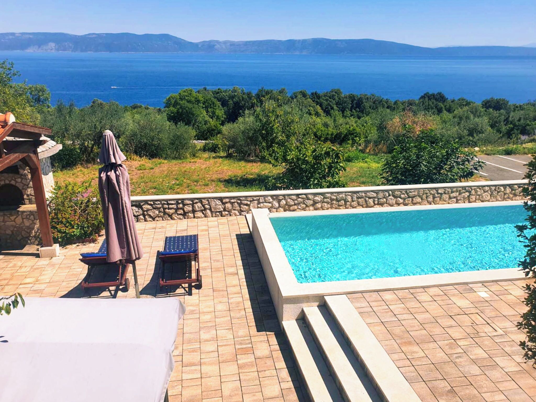 Una piscina amb un emmarcament de pedra, una zona de seients coberta i vista al mar.