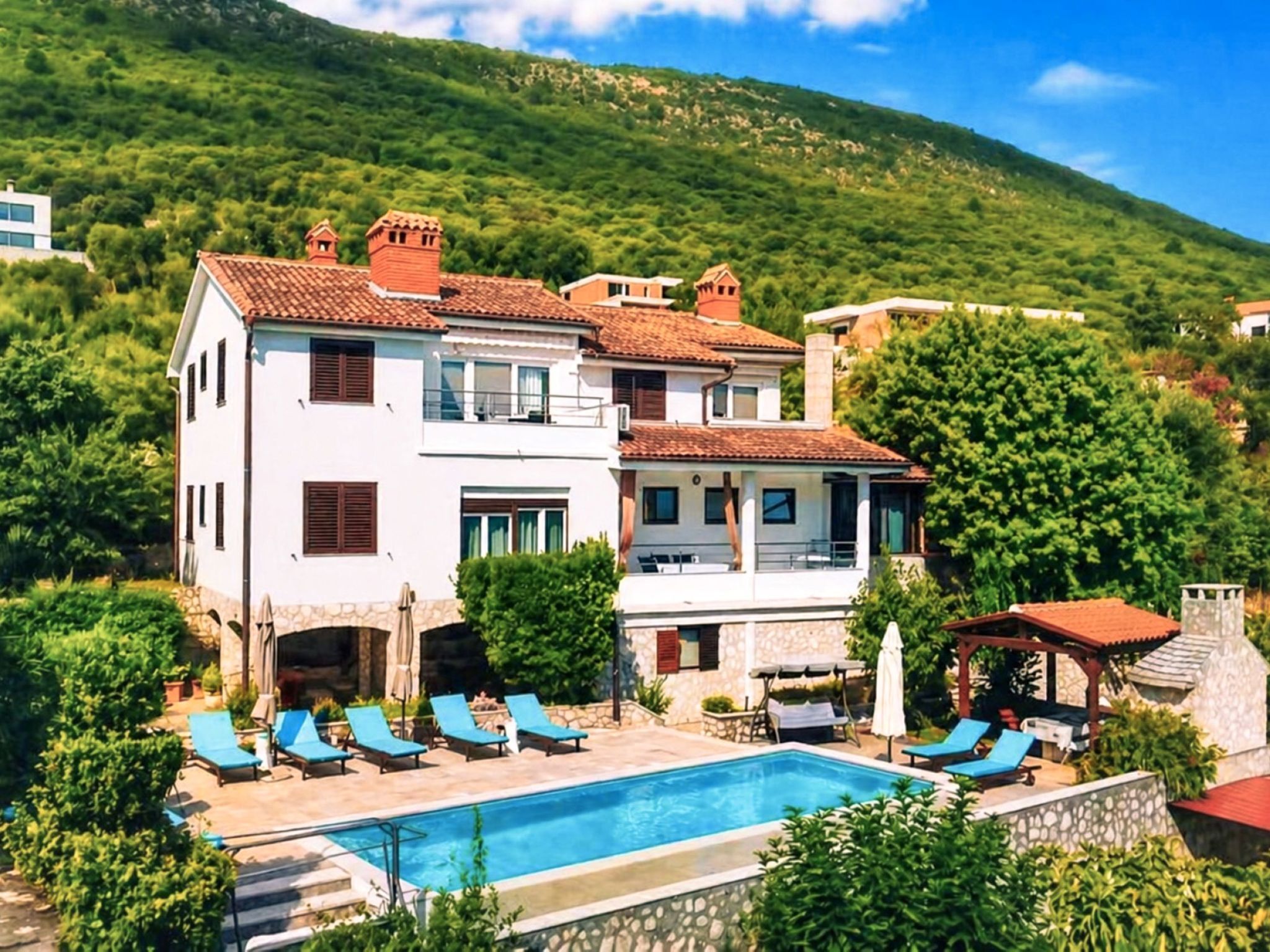 Une villa à deux étages dotée d’une piscine, de plusieurs chaises longues et offrant une vue sur une colline verdoyante.