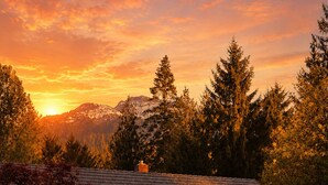Une cabane en rondins avec une cheminée, entourée d’arbres et avec des montagnes en arrière-plan.