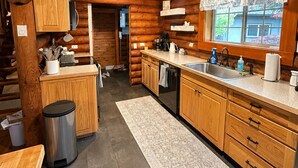 Une cuisine rustique aménagée dans une cabane en rondins, avec des meubles en bois, un évier en acier inoxydable et une fenêtre offrant une vue agréable.