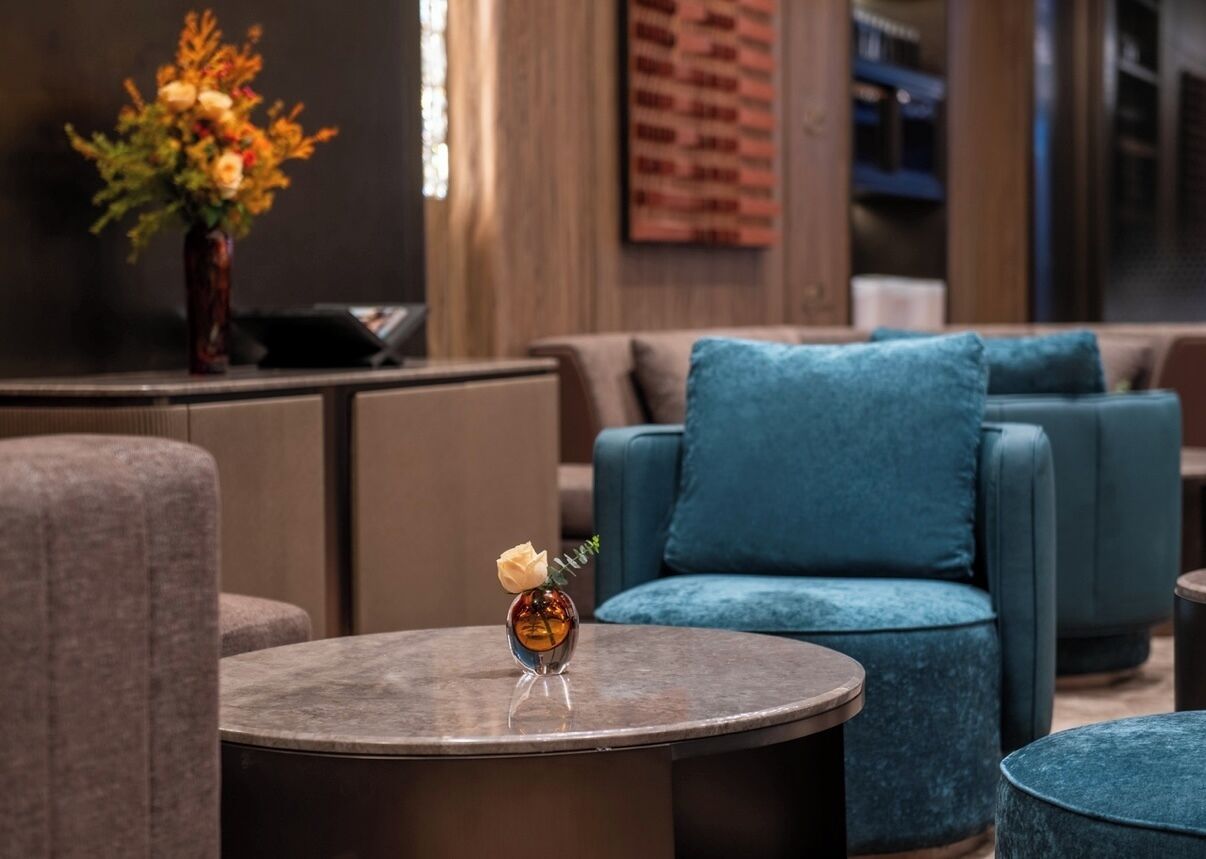 A modern lounge area with round tables, blue upholstered seating, and a vase with flowers.