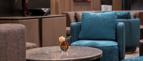A modern lounge area with round tables, blue upholstered seating, and a vase with flowers.