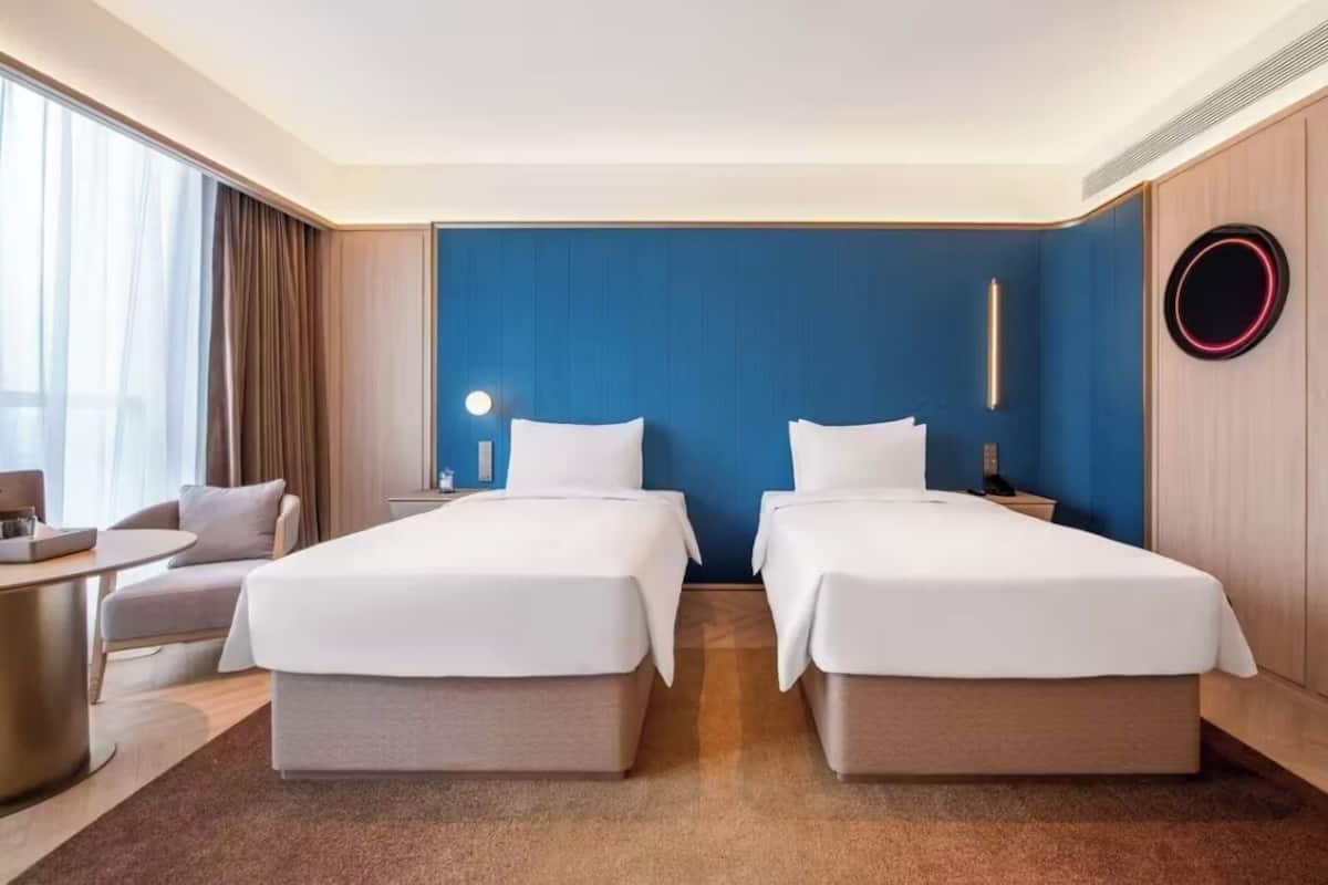 Ein Hotelzimmer mit zwei Betten, einem Schreibtisch, einem Stuhl und einem großen Fenster mit Vorhängen.