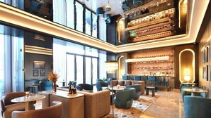 A modern hotel lobby with seating areas, a bar, and a view of the city.