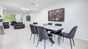 Amplia sala de estar con mesa de comedor, sillas negras, un conjunto de sofás y un ventanal grande.