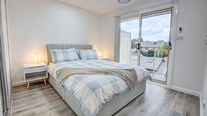 Un dormitorio con cama, mesitas de noche, una ventana y vistas al exterior.