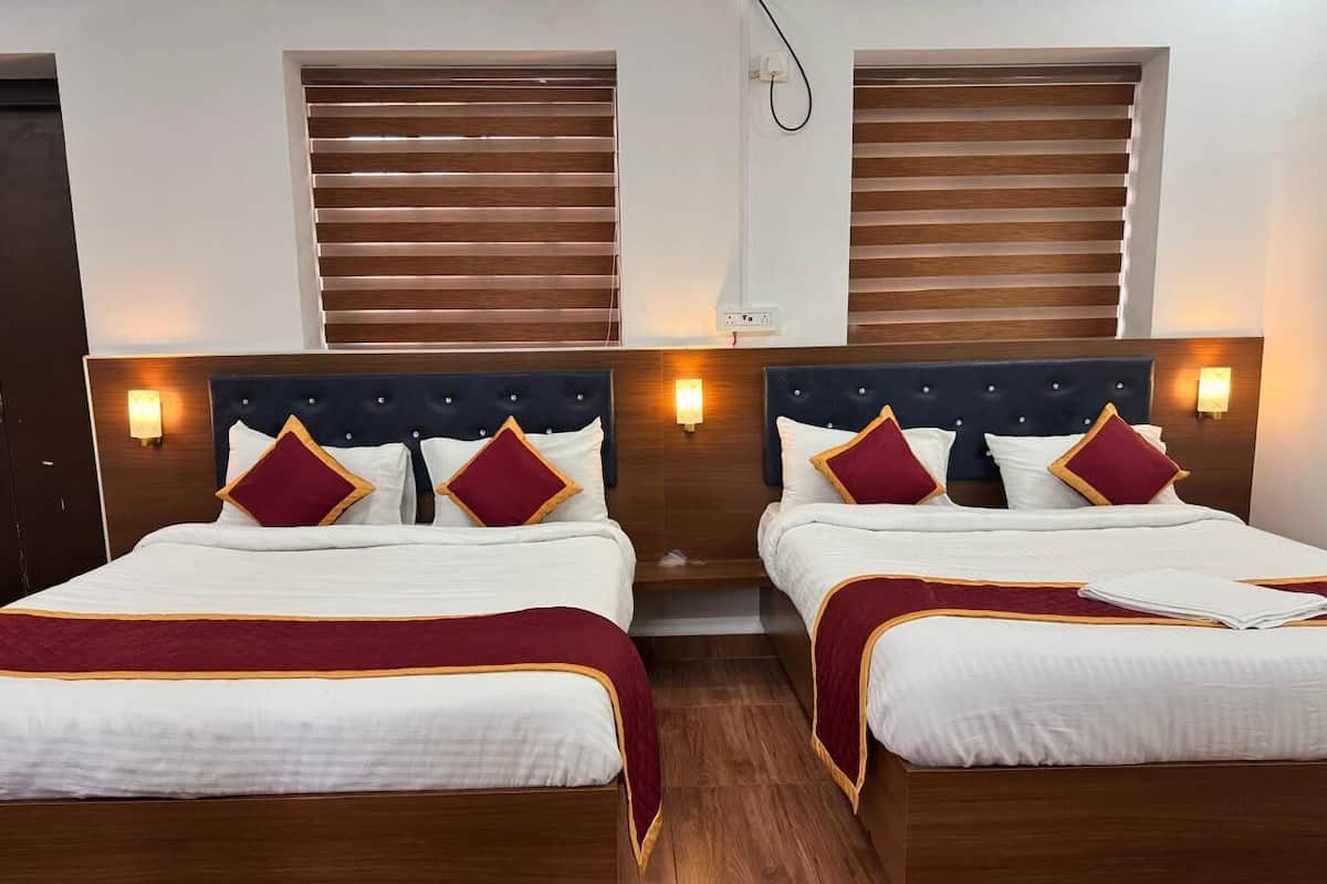 Duas camas de casal com cabeceiras de madeira, roupa de cama branca, detalhes em vermelho e dourado, e luminárias fixadas na parede.