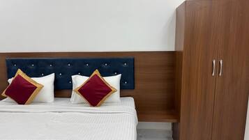 Una cama con cabecera capitonada, dos almohadas con detalles dorados y un armario de madera.
