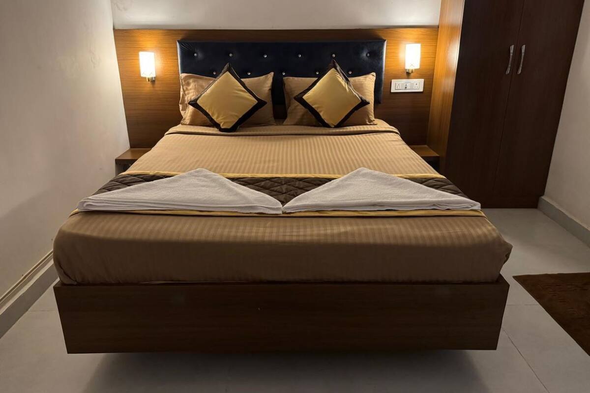 Uma cama grande com cabeceira escura, duas luminárias de cabeceira e um guarda-roupa de madeira.