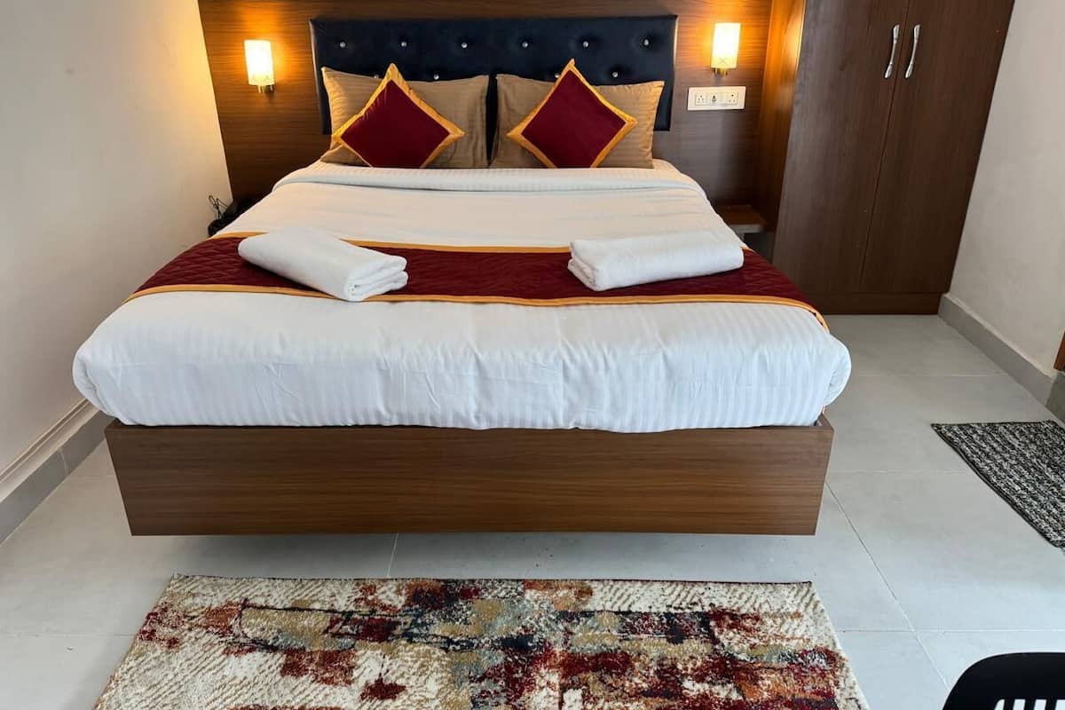 Uma cama bem arrumada com cabeceira, duas luminárias fixadas na parede e um guarda-roupa de madeira escura.