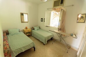 A small, clean room with two single beds, a nightstand, a radiator, and a window with curtains. - Nature Villa · Pool · Large Garden · Cap Bon (Grombalia)