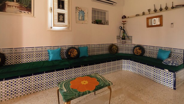 A room with a green sofa, patterned tiles, a decorative stool, and wall-mounted items. - Nature Villa · Pool · Large Garden · Cap Bon (Grombalia)