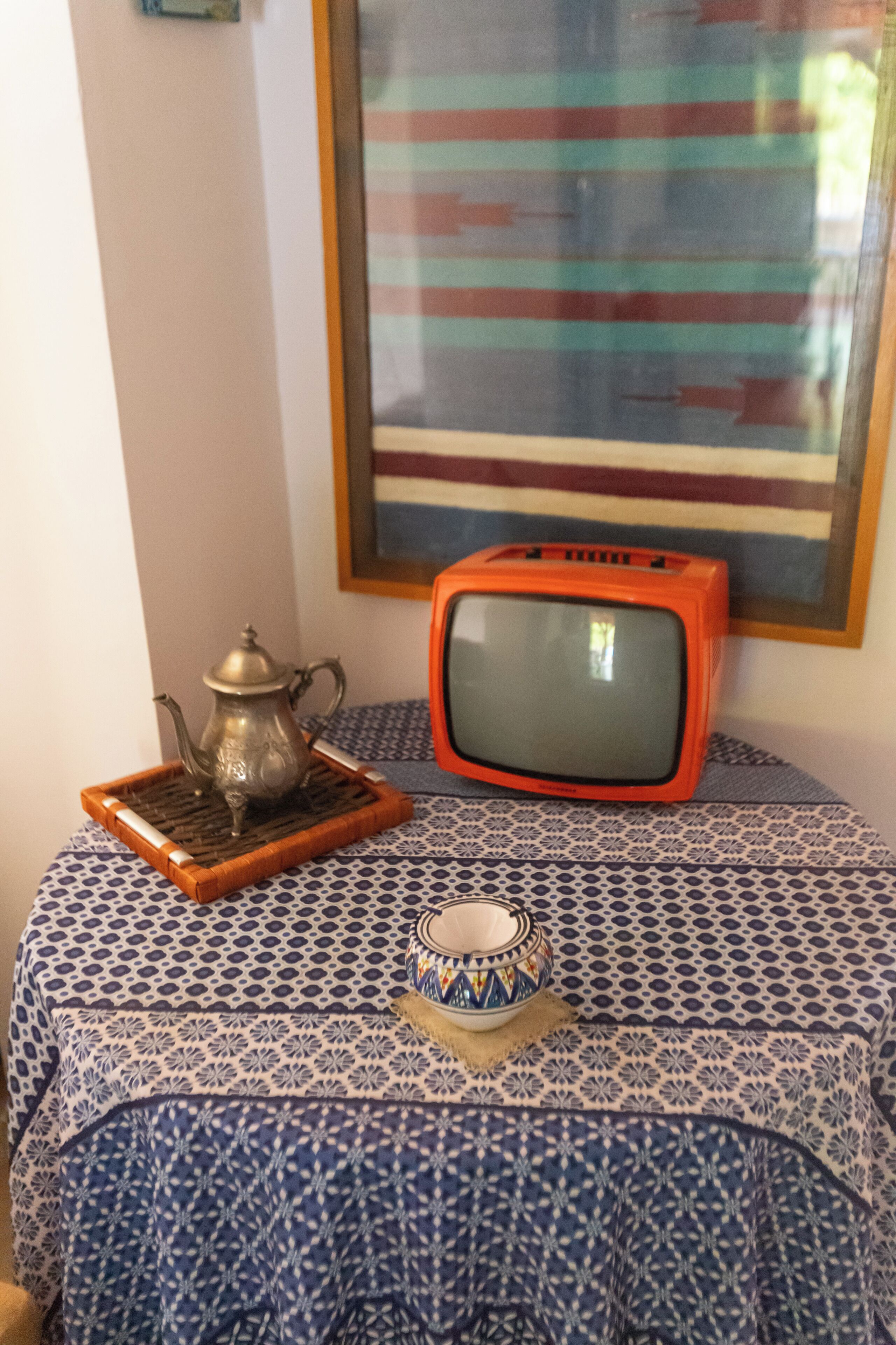 A room with a patterned tablecloth, a metal teapot, a small bowl, and a vintage television set.