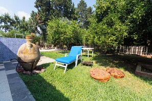 Ein Garten mit blauem Liegestuhl, einem großen Topf und einem kleinen Tisch.