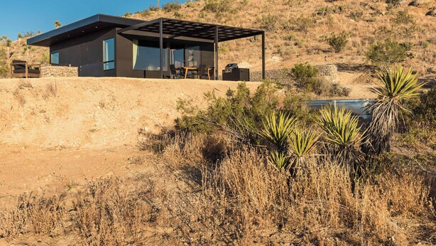 Une maison moderne dotée d’un patio, d’un mur en pierre et d’une végétation adaptée aux climats secs.