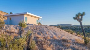 Une maison moderne avec un toit plat, de grandes fenêtres et une vue sur un paysage désertique.