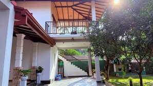 A covered outdoor area with a staircase leading to a balcony, surrounded by potted plants and a tree.