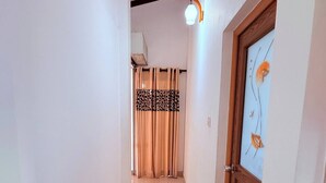 A hallway with a tiled floor, a wooden door with a glass panel, a striped rug, and a ceiling light fixture.