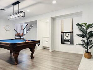 Een pooltafel in een ruimte met houten vloeren, een trap en een aan de muur bevestigd rack.
