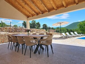 Eine Terrasse im Freien mit Tisch und Stühlen, einem Pool und Blick auf Berge.
