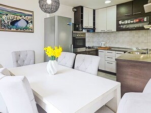 A modern kitchen with white cabinetry, a dining table with chairs, and a vase of yellow flowers. - Vacation home Smile by Interhome (Imotski)