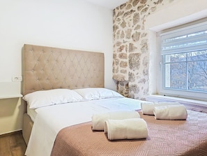 A bedroom with a tufted headboard, a stone wall, a window with a view, and neatly folded towels on the bed. - Vacation home Smile by Interhome (Imotski)