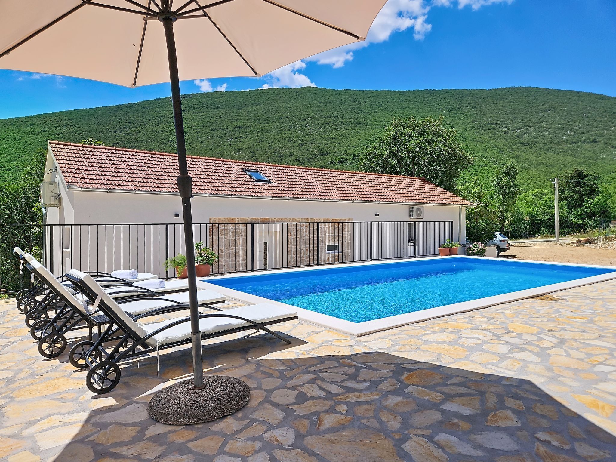 A poolside area with lounge chairs, a covered umbrella, and a view of a mountain.