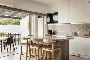 Una cocina moderna con una isla grande, taburetes de bar, una cafetera y un televisor montado sobre la encimera.