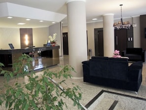 A hotel lobby with a reception desk, a black sofa, a chandelier, and a large pillar.