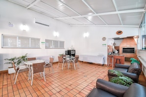 A dining area with a round table and chairs, a kitchen with a brick oven, and a seating area with sofas and a potted plant.