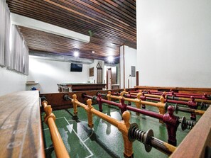 A room with a foosball table, a billiards table, and a television mounted on the wall.