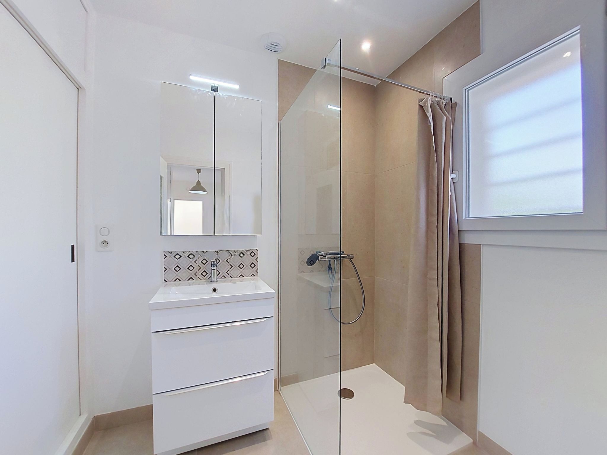 A modern bathroom with a glass shower enclosure, a white sink, and a mirror above it.