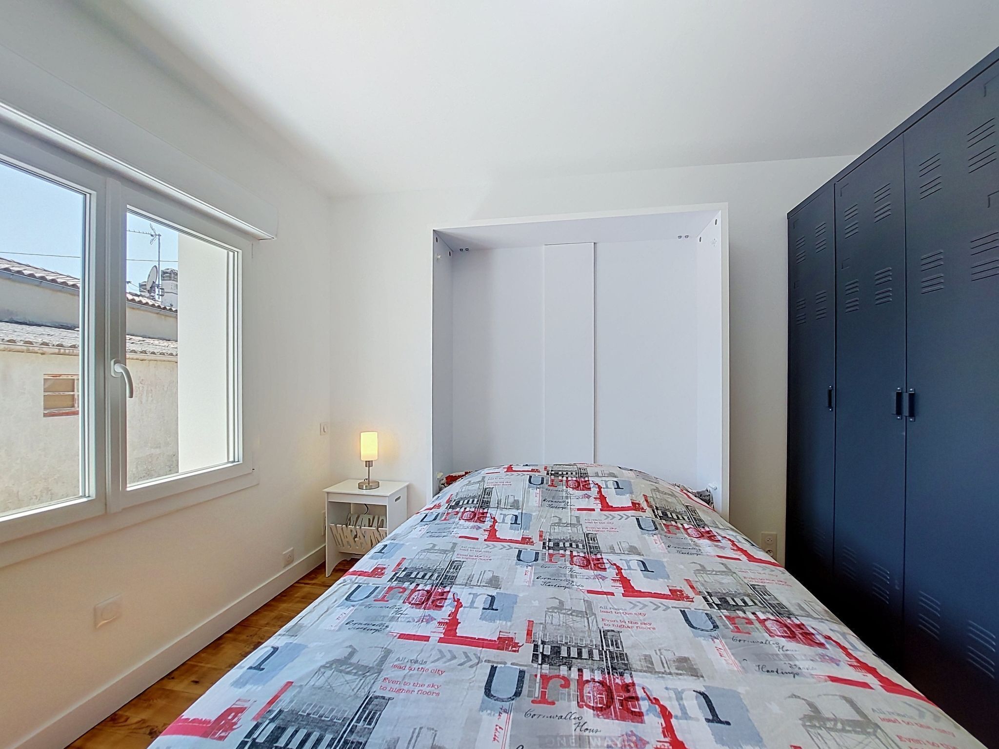 Un dormitorio con cama, mesita de noche, lámpara, armario y ventana.