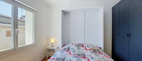 A bedroom with a bed, a nightstand, a lamp, a wardrobe, and a window.