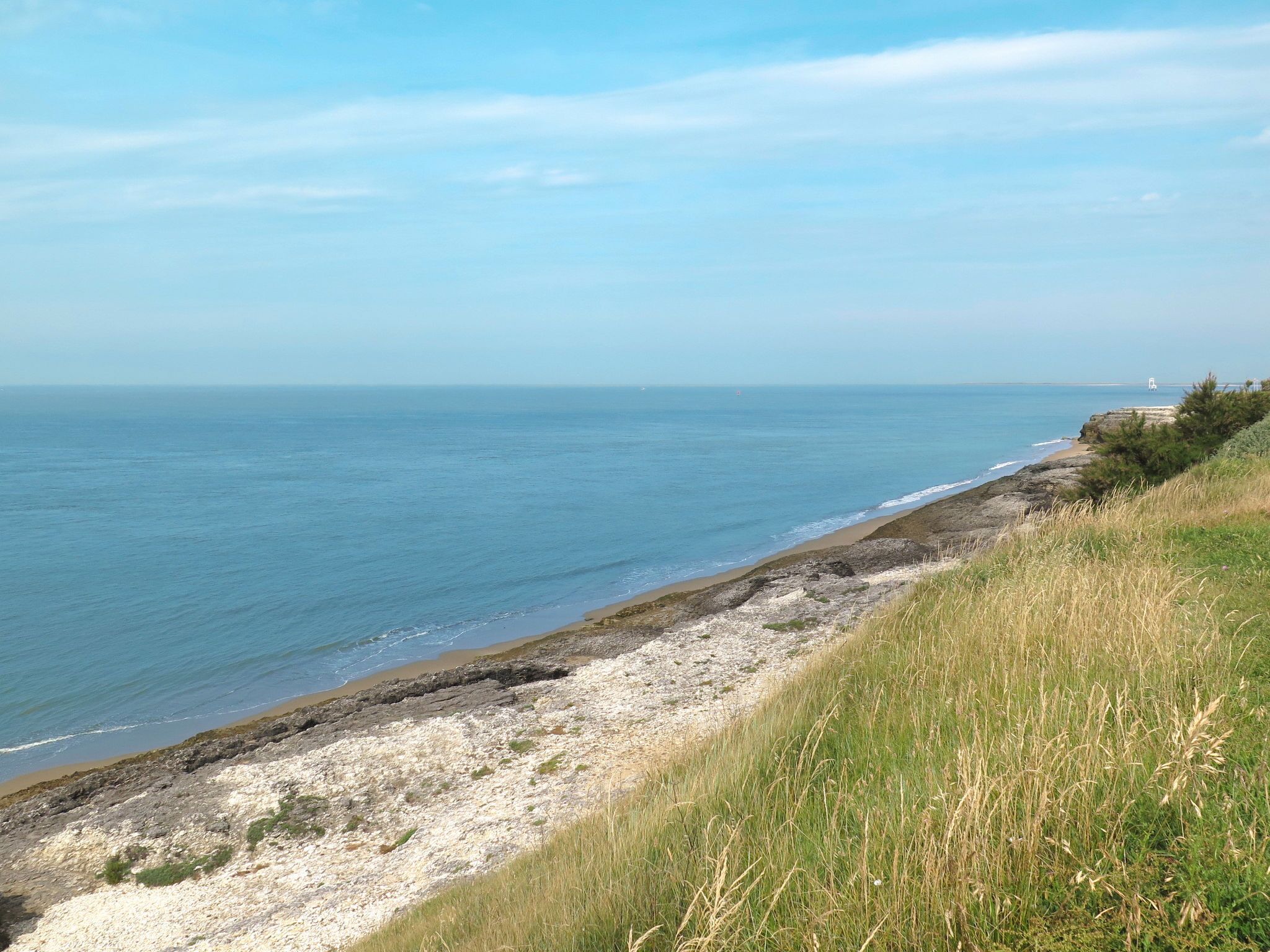 Eine Küstenlandschaft mit felsiger Küste, grünen Wiesen und freiem Blick auf das Meer.