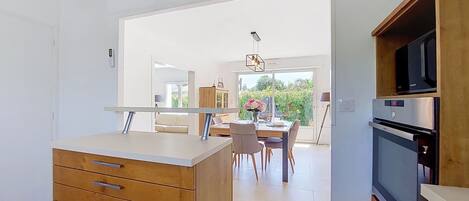 A modern kitchen with wooden cabinetry, a dining area with a table and chairs, and a view of the outdoors.