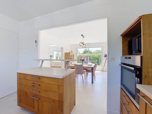 Eine moderne Küche mit Holzschnitzerei, ein Essbereich mit Tisch und Stühlen und ein Blick ins Freie.