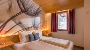 A bedroom with a bed, bedside tables, a lamp, a window with curtains, and a wall with a large abstract design.