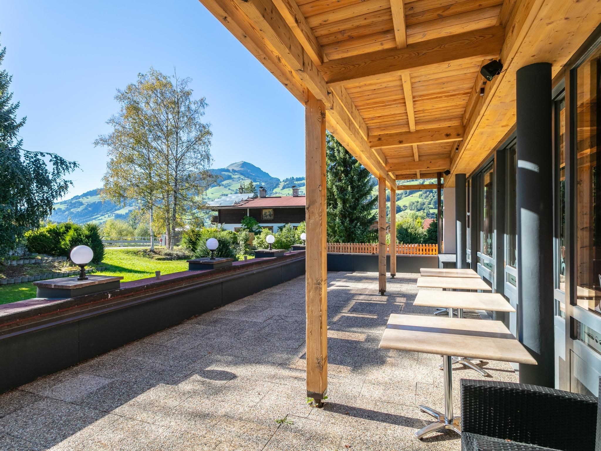 A covered outdoor seating area with tables and chairs, a gravel ground, and a view of a mountain landscape.